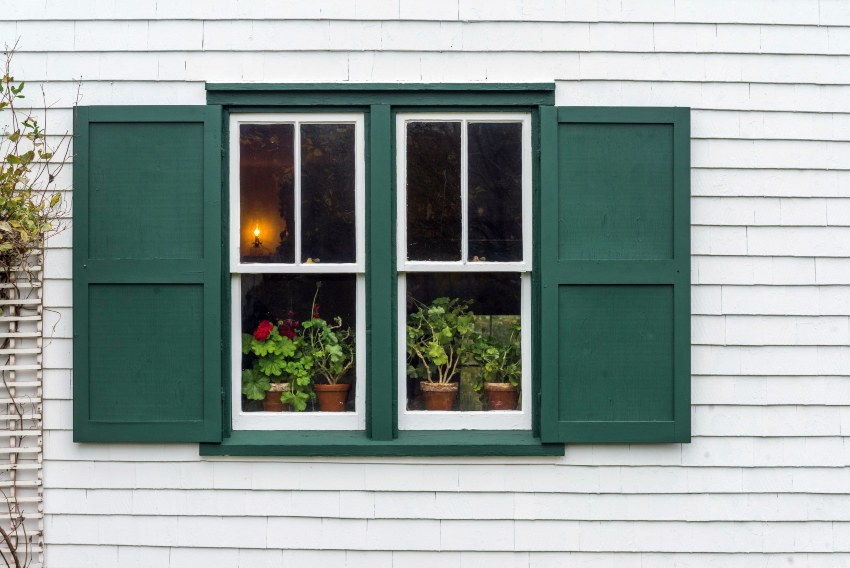 A double hung window with green shutters and potted plants in Salem, NH