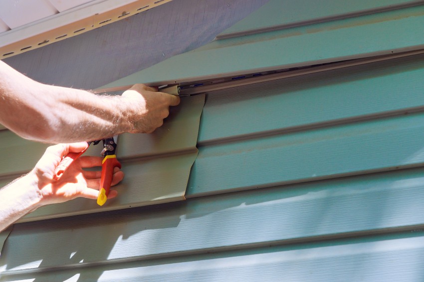 A man is installing vinyl siding with pliers in Salem, NH