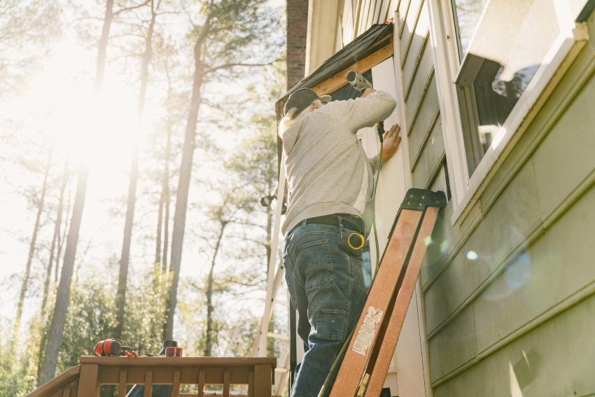 A man is using a ladder and installing siding on a house in Salem, NH